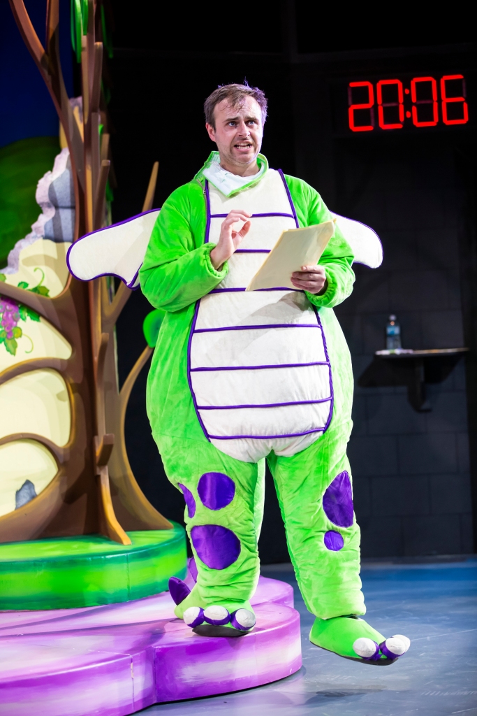 shows 'Andy' (Adam Byron) wearing a bright green with purple dots dragon body custom, holding a yellow script.