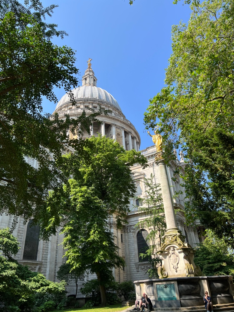A outside summer photo of St Paul’s Cathedral a white building with a dome on top with some green trees in the foreground.